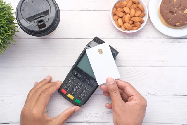 Hands making a contactless payment with a credit card on a wooden table. Acquéreur et prestataire de services de paiement : qui fait quoi lors des paiements par carte en Suisse